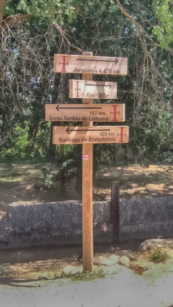 Un poste con varias señales indicando la distancia a lugares santos