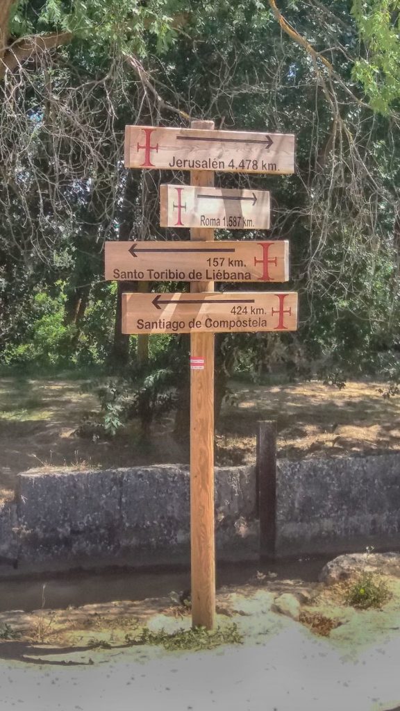 Un poste con varias señales indicando la distancia a lugares santos