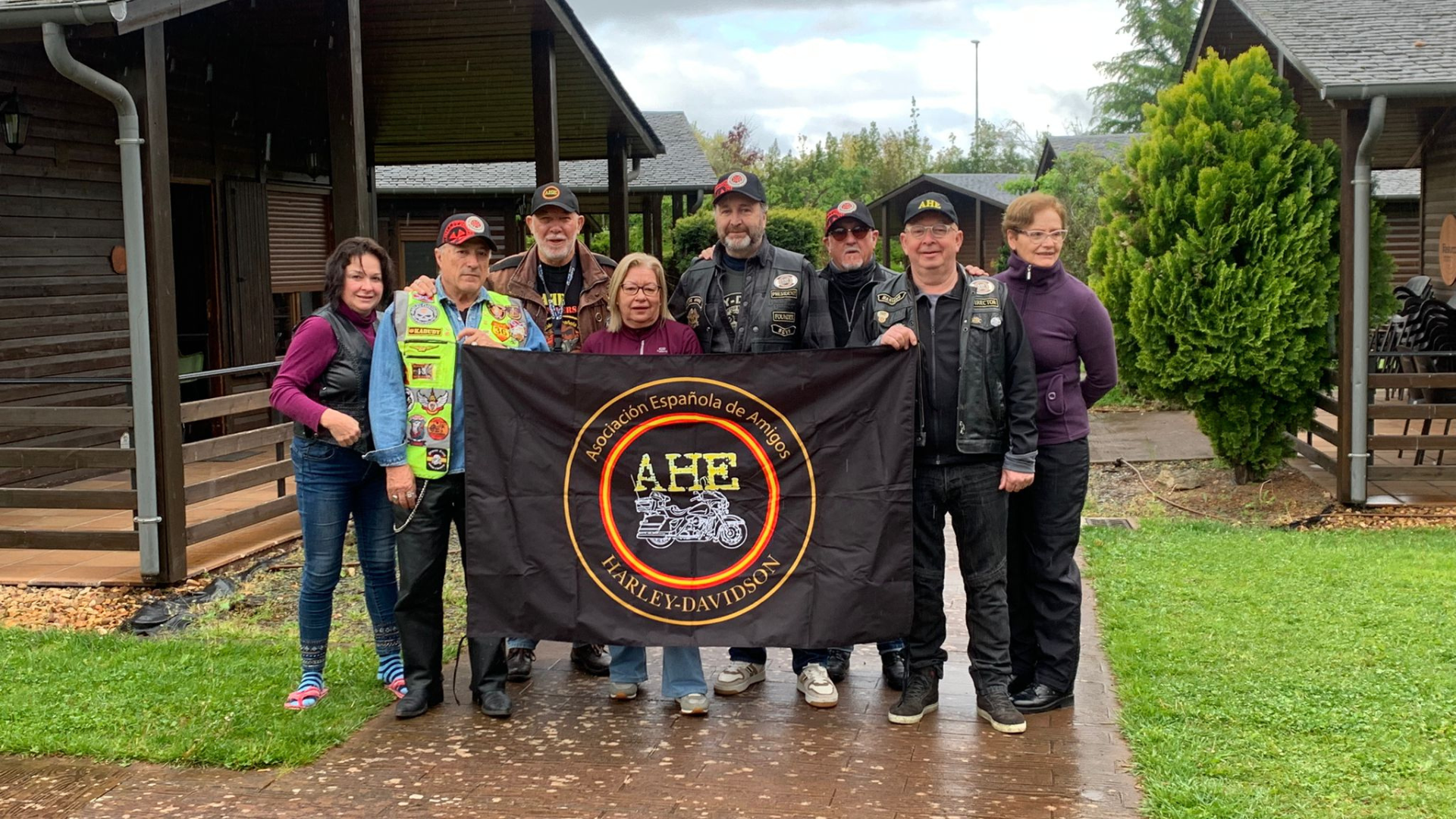 Un grupo de moteros posan frente a las cabañas de El Bosque de los Sueños con una bandera de su asociación